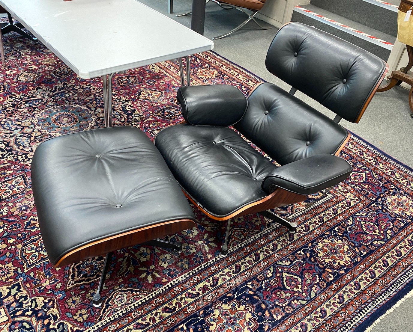 A pair of Eames style black leather, simulated rosewood swivel lounge chairs and footstools